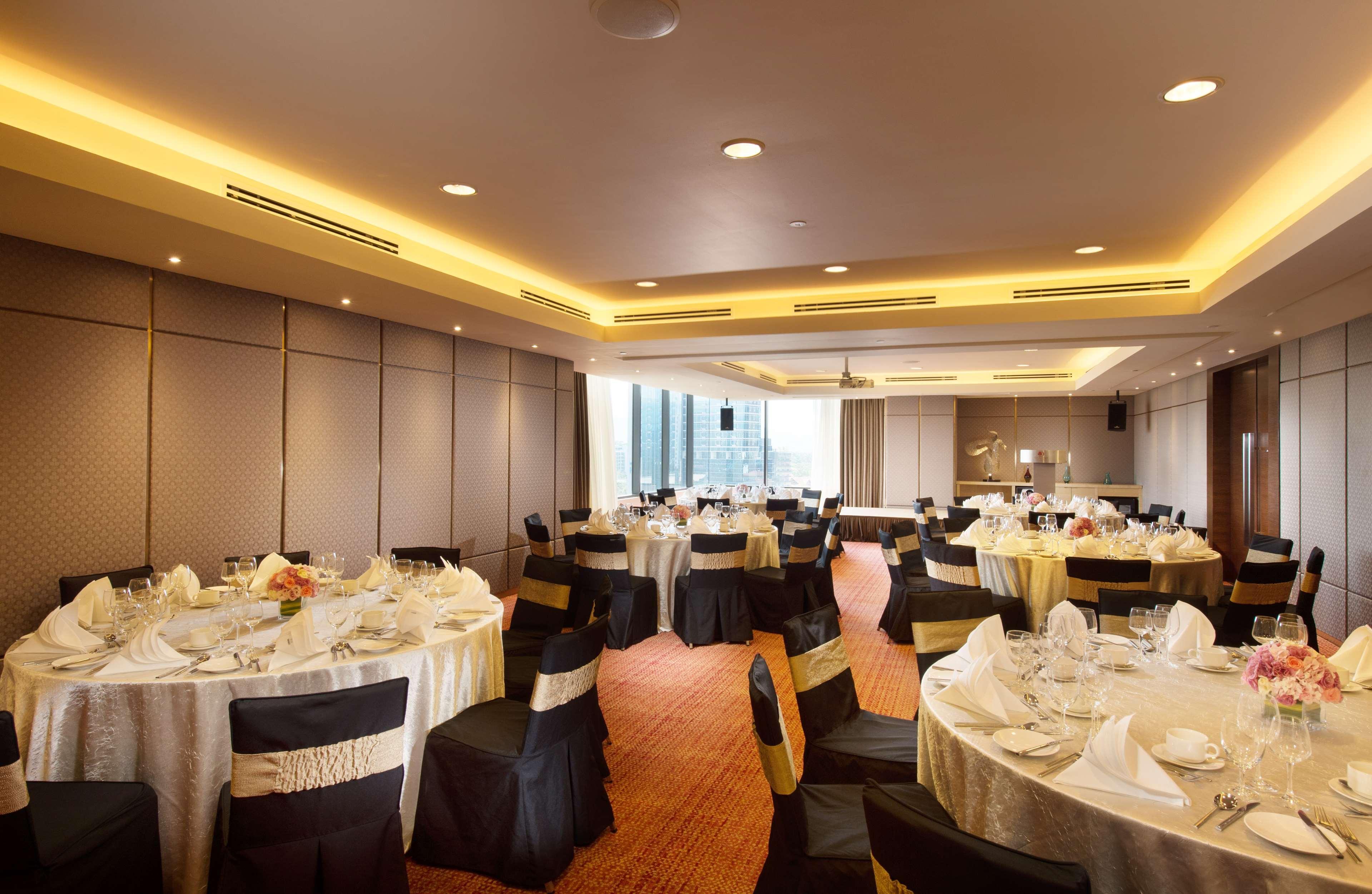 Doubletree By Hilton Kuala Lumpur Exterior foto The photo depicts a decorated banquet hall or event space. There are several round tables set with white tablecloths and black chair covers, some adorned with gold sashes. Each table is elegantly arranged with tableware, including plates, glassware, 