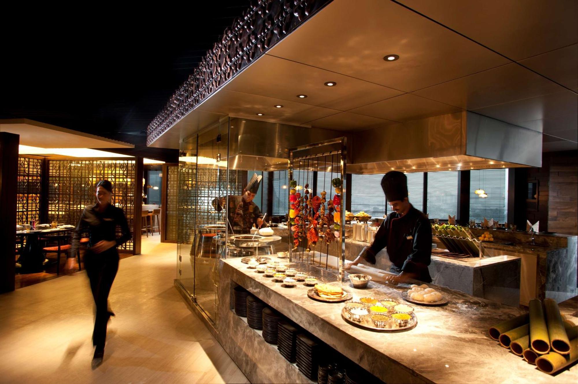 Doubletree By Hilton Kuala Lumpur Exterior foto The photo depicts a modern restaurant interior with a sleek and sophisticated design. In the foreground, there is a chef working at an open kitchen area, preparing food. The kitchen features a glass display that showcases a variety of dishes, along w