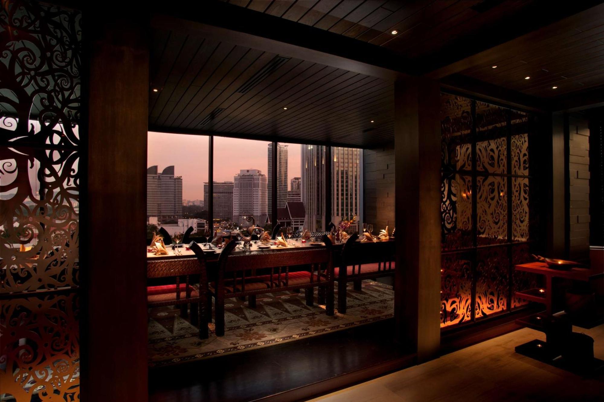 Doubletree By Hilton Kuala Lumpur Exterior foto The photo depicts a modern dining area in a restaurant, featuring a long table set for a meal. The room has a warm, inviting atmosphere, illuminated by soft lighting. Large windows provide a view of the city skyline, possibly during sunset, creating 