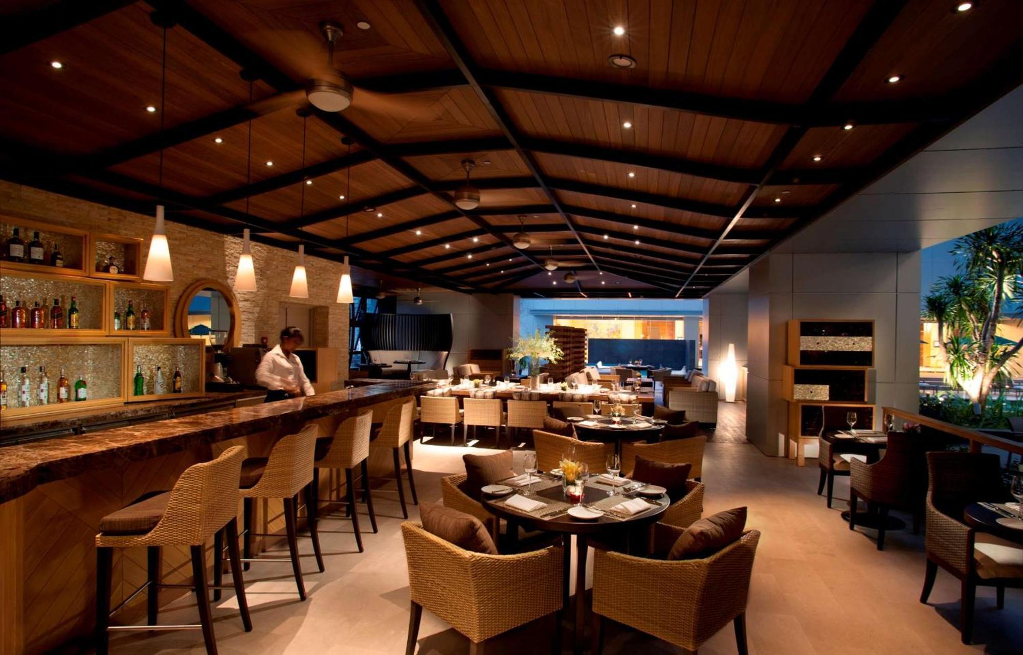 Doubletree By Hilton Kuala Lumpur Exterior foto The photo shows an upscale restaurant interior with a warm and inviting ambiance. There is a large wooden bar area on one side, with bar stools arranged around it. The ceiling features wooden beams and modern lighting fixtures, creating a cozy atmosp