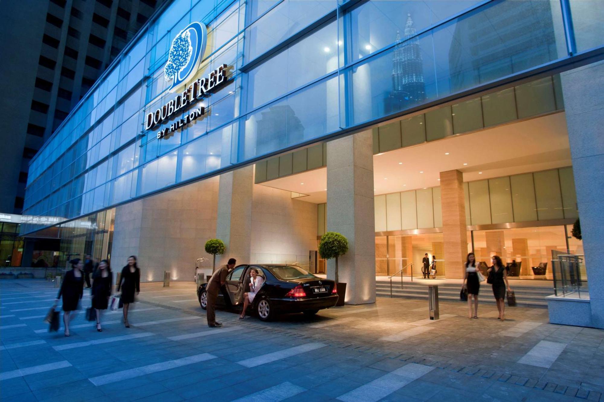 Doubletree By Hilton Kuala Lumpur Exterior foto The photo shows the exterior of a DoubleTree hotel. The building features a modern glass facade with the hotel’s logo prominently displayed. In front of the entrance, there is a black car parked, and a few people can be seen, possibly arriving or lea