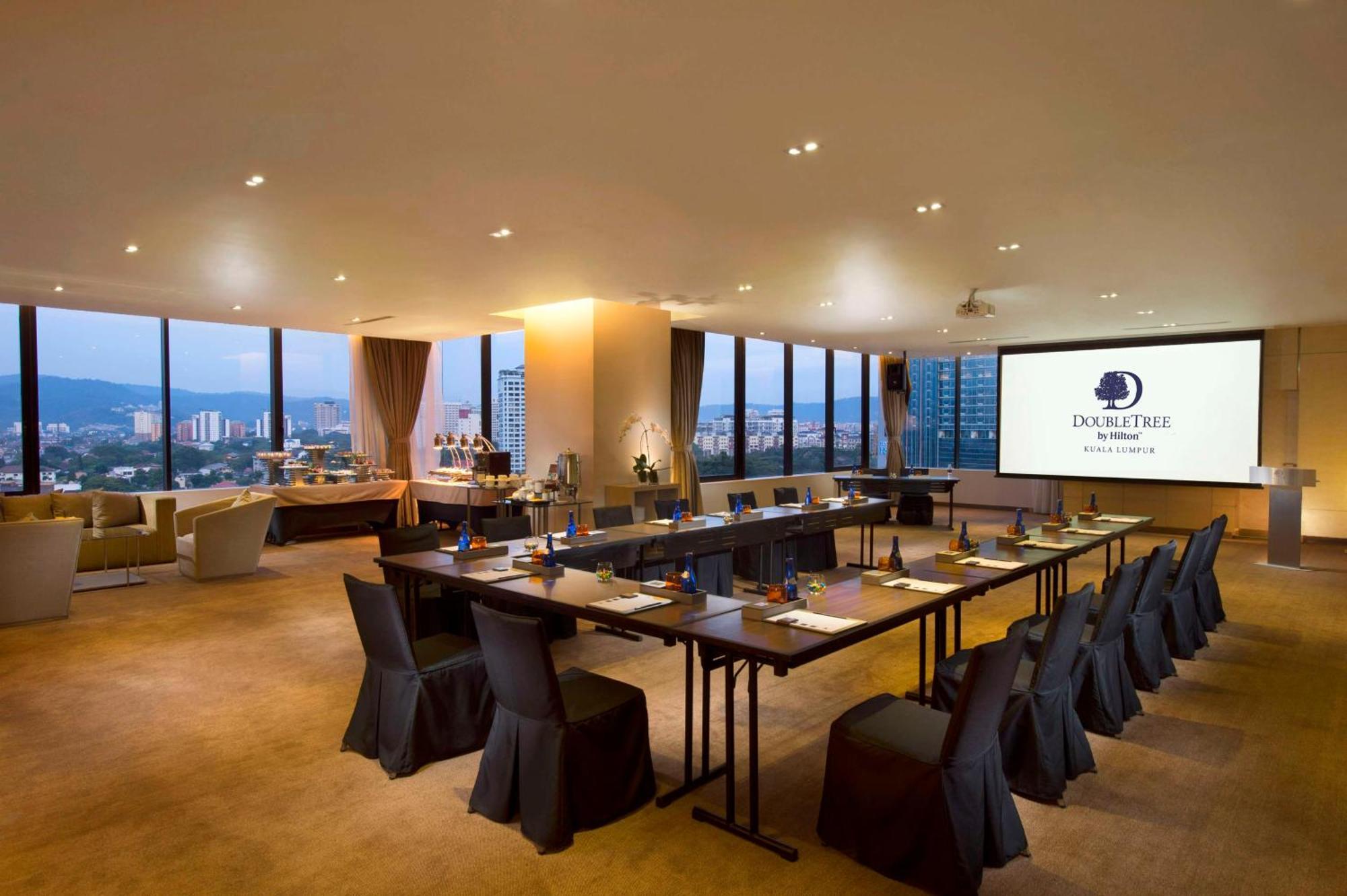 Doubletree By Hilton Kuala Lumpur Exterior foto The photo shows a modern conference room. It features a long table arranged for a meeting, with black chairs and notepads placed at each seat. The room has large windows that let in natural light and offer a view of the city outside. On one wall, the